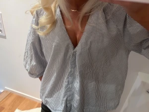 Randig v-ringad skjorta med knappar - Snygg skjorta med smala blå och vita ränder, v-ringning och knappar framtill. Skjortan har trekvartsärmar och en lite loose passform, perfekt för en chill och stilren look.