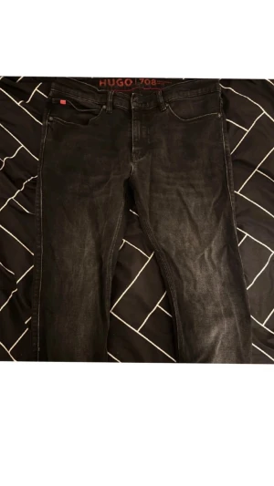 Svarta jeans från Hugo med röd patch - Snygga svarta jeans från Hugo med en cool röd patch bak och diskreta logodetaljer. Klassisk femficksmodell med raka ben och normal passform. Jeansen är tillverkade i slitstarkt denim och har svarta sömmar för en clean look.