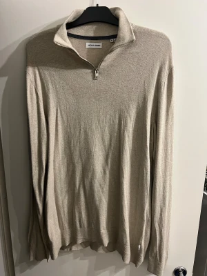 Beige half zip tröja Jack & Jones XL - Snygg beige långärmad tröja från Jack & Jones i storlek XL. Tröjan har en stilren half zip-dragkedja vid kragen och är tillverkad i mjuk bomull. Perfekt för dig som gillar enkel och clean stil med lite extra edge i detaljerna.