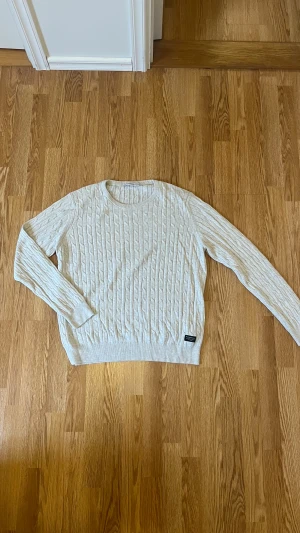 Beige kabelstickad tröja Peak Performance - Snygg beige kabelstickad tröja från Peak Performance i storlek XL. Tröjan har rund hals, ribbade muddar och ett klassiskt kabelmönster över hela plagget. Perfekt för dig som gillar stilrena och tidlösa plagg med lite extra struktur.