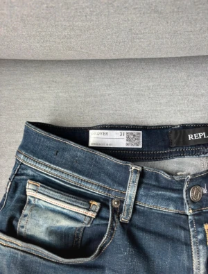 Replay Grover Hyperflex jeans blå - Snygga Replay Grover Hyperflex jeans i mörkblå tvätt med slitningar och kontrastsömmar. Klassisk femficksmodell med läderpatch bak och coola detaljer på bakfickorna. Stretchigt material för extra komfort och passform. Dom är uppsydda till 31/30