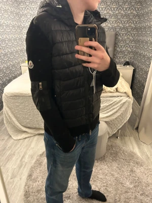 Moncler Cardigan  - Svart cardigan från Moncler i storlek L med stickade ärmar och huva. Jackan har dragkedja framtill, två sidofickor med knappar och en ficka med dragkedja på ärmen. Moncler-logga på vänster ärm. Snygg, stilren och perfekt för kalla dagar som dessa. Tagg funkar. Säljer den pga att den är på gränsen för liten för mig