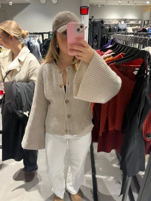 Beige kofta från Wakakuu Icons - Säljer en snygg greige kofta från Wakakuu Icons med breda, långa ärmar och ribbad struktur. Koftan har rund hals, stora beige knappar och är tillverkad i en lyxig mix av kashmir, merinoull och viskos. Perfekt för dig som gillar stilrena och trendiga plagg. Original pris är 2500kr!💕 Fint skick! 