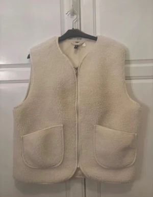 Slutsåld teddyväst ifrån H&M - Teddyväst från H&M med två stora framfickor och dragkedja. Västen har en rundad hals och är tillverkad i mjukt, fluffigt material. Perfekt att slänga över en hoodie eller stickad tröja när det är lite kyligt ute. Den är i nyskick och endast använd 2 gånger. Helt slutsåld! 😇💖