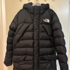 Svart pufferjacka från The North Face - Säljer en svart pufferjacka från The North Face med huva och logga på bröstet. Jackan har dragkedja, kardborre och flera fickor, inklusive en innerficka med dragkedja. Perfekt för kalla dagar och riktigt snygg streetstil.