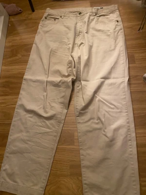 Beige raka jeansbyxor. - Snygga beige byxor med klassisk femficksdesign och raka ben. Byxorna har normal passform, bälteshällor och metallknappar. Perfekt för dig som gillar stilrena och enkla plagg i bomull. Passar till sneakers eller boots.