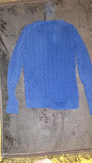 Blå kabelstickad tröja från Gant - Kabelstickad blå tröja från Gant i storlek M. Tröjan har rund halsringning, ribbade muddar och Gant-logga broderad på bröstet. Perfekt för lager-på-lager och en klassisk preppy stil.