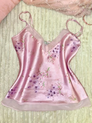 Satin linnetopp - Säljer en populär kategori, en  ljusrosa linnetopp i satin med blommigt mönster i lila och lite grönt. Toppen har smala axelband och v-ringad hals. Sval och glansig känsla, passar till många olika looks.  Jag köpte den från en italiensk Lingerie butik , tror märket stavas Emotion 🩷 