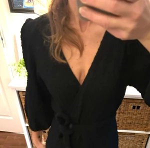 Svart omlottklänning från Indiska fest julfin Stl m - Säljer en svart omlottklänning från Indiska i storlek M. Klänningen har v-ringning, knytband i midjan och trekvart puffärmar vid ärmslut. Materialet är strukturerat och känns mjukt mot huden. Perfekt för dig som gillar en enkel men snygg look. Använd 2 ggr