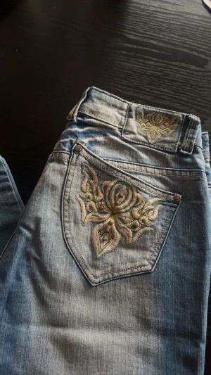 Blå jeans med broderad ficka Jenny B. - Säljer dessa snygga blå jeans från Jenny B. med broderad detalj och nitar på bakfickan samt broderi vid linningen. Jeansen har klassisk femficksdesign och är tillverkade i stretchig bomull med 3% elastan för skön passform.