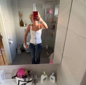 Vit randig korsett med snörning - Säljer en vit korsett-topp från Zara med tunna svarta ränder och snygg snörning framtill. Toppen har breda axelband och är figurnära med en croppad passform. Perfekt för dig som vill ha en trendig och edgy look. Materialet känns som bomull eller polyester.