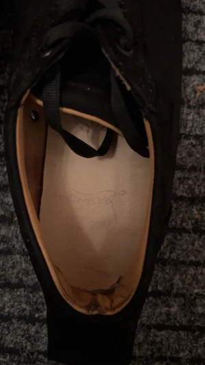 Svarta Louboutin sneakers med nitar - Säljer ett par svarta sneakers från Christian Louboutin med ikonisk röd sula och svarta nitar på tån. Skorna har snörning och är tillverkade i skinn och textil. Riktigt edgy och sticker ut med sin coola design och detaljer. Kan även tradea mot ett par utan spikade!! Köpte för 2500 i september 