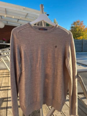 Beige stickad tröja från Morris - Snygg beige stickad tröja från Morris med diskret logga broderad på bröstet. Tröjan har rund hals, ribbade muddar och lång ärm. Perfekt för dig som gillar stilrena och klassiska plagg med en chill vibe. Passar mer S men storlek M. OBS Köper du den för fullpris får du med en Skjort jacka gratis 