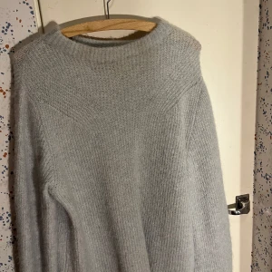 Ljusgrågrön stickad tröja - Ljusgrå stickad tröja med rund hals och långärmad design. Tröjan har en enkel, ribbad struktur och är perfekt för att hålla värmen under kyliga dagar. Tröjan är i en ljusgrön färg!