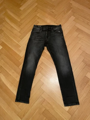 Svarta slim jeans från G-Star RAW - Snygga svarta jeans från G-Star RAW, modell 3301 Slim. Diskret logotyp på fickan. Materialet är jeans med en mörk tvätt och smal passform som sitter tajt längs benen. Dessa är köpta för 1200 nypris och använda vid ett fåtal tillfällen. Storlek 28/30. Bara att höra av sig vid funderingar 