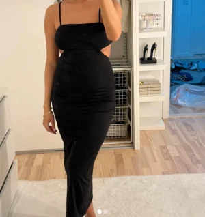 Svart långklänning med öppen rygg - Snygg svart långklänning med smala axelband och öppen rygg. Klänningen har en figurnära passform och stilren design som ger en modern och cool vibe. Perfekt för dig som gillar minimalistiskt och trendigt. Materialet känns mjukt och följsamt mot kroppen.
