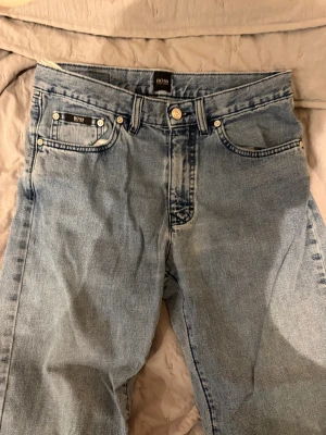 Ljusblå jeans från Hugo Boss W31 L32 - Säljer ett par ljusblå jeans från Hugo Boss, modell Arkansas. Klassisk femficksdesign med Boss-logga på fickan och bakre läderpatch. Jeansen är raka i modellen och har normal passform. Materialet är 100% bomull för en skön känsla.