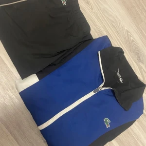 Lacoste tracksuit - Säljer Lacoste tracksuit  med blå sidopaneler och broderad logga framtill. Shortsen har elastisk midja med snörning för skön passform. Perfekta för sport eller chill dagar. Klassisk Lacoste-stil med tydlig krokodillogga. Finns inte att köpa i butik längre Och nypris 3500kr                                   MÖTS I STOCKHOLM🙃