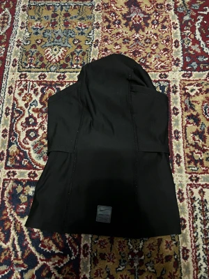 Svart Nike Pro hoodie med huva - Svart hoodie från Nike Pro med stilren design och huva. Tröjan har en tight passform och är tillverkad i ett stretchigt syntetmaterial som passar perfekt för träning. Nike-logga på bröstet och etikett nedtill. Snygg och sportig look för gymmet eller löprundan.