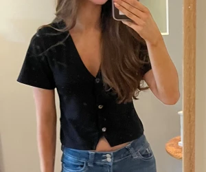 Svart croppad blus från 157 - Svart blus från 157 i storlek S. Modellen är croppad med korta ärmar, v-ringning och knappar framtill. Toppens stil är enkel och clean, perfekt för dig som gillar minimalistiska looks. Materialet känns mjukt och lätt mot huden.