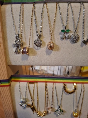 Mixade halsband med hängen - Säljer flera halsband med olika hängen, bland annat kors, körsbär med gröna blad, blommor, pärlor och geometriska former. Kedjorna är i silver- och guldfärg, vissa med glittriga detaljer och stenar. Perfekt för dig som gillar att variera din stil med unika smycken.