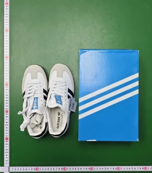 Adidas Samba sneakers vit/svart - Adidas Samba sneakers i klassisk vit och svart färg med bruna gummisulor. Skorna har svarta ränder på sidorna, snörning och rund tå. Ovandelen är i skinn och mocka med blå Adidas-logga på plösen. Perfekt för dig som gillar retrostil och sportig vibe.