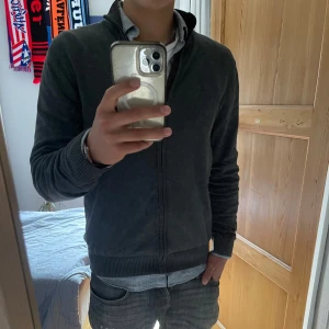 Mörkgrå fullzip från Dressmann - | Säljer en mörkgrå fullzip från Dressman | Använd men den är i utmärkt skick - 9/10 | storlek L - sitter bra på mig som är 187 | Nypris runt 800 mitt pris 299 kr | Bra plagg nu till sommaren att bära till exempel över en skjorta som jag har i bilden en sommarkväll |