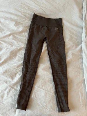 Gymshark träningstights  - Snygga bruna seamless tights från Gymshark med hög midja och stretchigt material som sitter tight och bekvämt, perfekt för gymmet eller löpning. Helt oanvända, passade inte mig i storleken! Modellen på tightsen är vital seamless 2.0 och färgen heter Brown Marl
