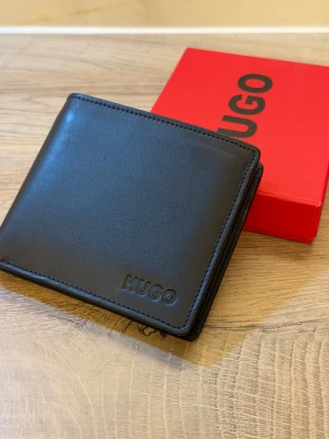 HUGO Subway 4CC genuine leather wallet. - HUGO Subway 4CC genuine leather wallet.  Compartments: Coin compartment, card slots, slip compartment, note compartment .An elegant wallet , designed with four card slots and a coin pocket. Featuring a soft grain and matte effect, this wallet is embossed with logos inside and out for plenty of signature appeal.  Height: 9.5 cm  Length: 11 cm  Width: 2 cm   Fully lined Embossed logo  New with Tags And Original Box & tissue 