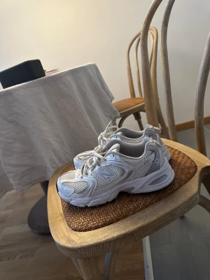 Vita New Balance 530 sneakers - Säljer ett par fräscha New Balance 530 sneakers i vitt med silverdetaljer. Skorna har meshpaneler för extra ventilation, snörning och en chunky sula med ABZORB-dämpning. Perfekt för dig som gillar retrostil och sportig vibe.