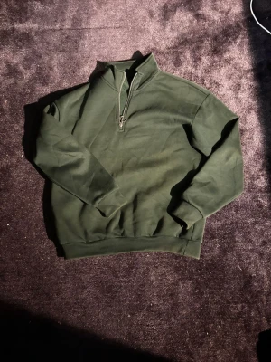 Mörkgrön half zip sweatshirt - Mörkgrön sweatshirt med half zip och hög krage. Tröjan har en relaxed passform och är tillverkad i mjukt bomullsmaterial. Perfekt för lager-på-lager och chill dagar. Långa ärmar och breda muddar vid ärmslut och nederkant.