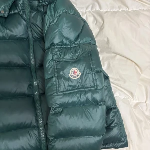 Moncler Maya - Skitsnygg grön moncler maya jacka som är perfekt nu inför kommande kalla månader. Köpt förra året när den var ny här på Plick och används alltså endast i vintras. Dragkedjan på innerfickan funkar inte och kvitto saknas därav de låga priset. Inga skavanker förutom de och perfekt jacka för kylan. Snyggare jacka finner du inte. Vid frågor tveka inte på att skriva. Pris går absolut att diskuteras 🙌