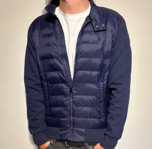 Marinblå pufferjacka från Polo Ralph Lauren - Snygg marinblå pufferjacka från Polo Ralph Lauren med quiltad front och mjuka ärmar i bomull. Jackan har dragkedja, ståkrage med tryckknappar och två fickor fram. Perfekt för dig som vill ha en stilren och sportig look.