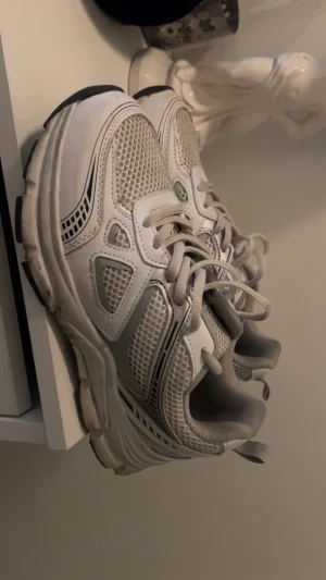 Vita mesh-sneakers med snörning - Populära vita sneakers med mesh-paneler och detaljer i grått från Lager157. Skorna har rund tå, platt sula och klassisk snörning. Perfekt för dig som gillar sportig stil och vill ha bekväma skor till vardagen. Materialet är syntet och mesh för extra ventilation.