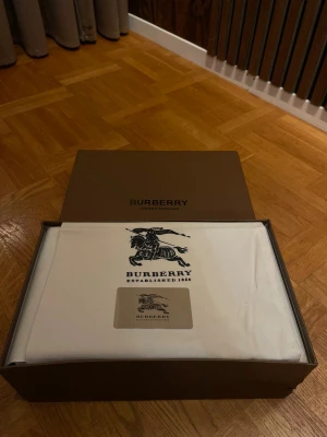 Burberry sneakers med rutig detalj - Snygga Burberry sneakers med svart skinn och mocka på ovandelen, vit platt sula och klassisk rutig panel i beige, svart och brun på sidan. Skorna har rund tå och snörning, och den ikoniska Burberry-looken gör dem riktigt stilrena.