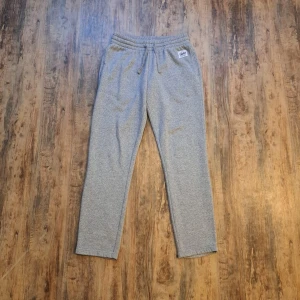 Grå mjukisbyxor - Frank Dandy - Grå mjukisbyxor från Andy by Frank Dandy med elastisk midja och snörning. Byxorna har raka ben och en enkel, stilren look. Perfekta för chill dagar eller när du vill vara bekväm. Mjukt material i bomullsblandning och diskret logga framtill.