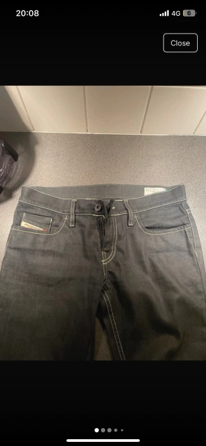 Svarta Diesel jeans med kontrastsömmar - Snygga svarta jeans från Diesel med tydliga kontrastsömmar och klassisk femficksdesign. Modellen har raka ben och normal passform, med Diesel ä-logga på myntfickan och broderade bakfickor. Perfekt för dig som gillar stilrena jeans med detaljer.