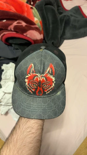 Gucci keps med röd vargtryck - PRIS KAN DISKUTERAS.                          Snygg Gucci keps i svart och grått med GG-monogram och ett fett rött vargtryck framtill. Mesh på sidorna och justerbar rem med röd detalj bak. Märkt med Gucci-tag på insidan. Perfekt för dig som vill sticka ut med designer vibes.