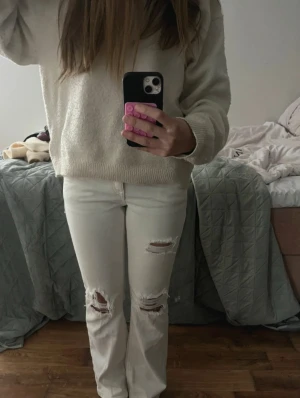 Vita ripped jeans från Gina Tricot - Säljer ett par vita jeans från Gina Tricot med snygga slitningar på knäna och låren. Modellen har raka ben och klassisk femficksdesign med knappar bak. Jeansen är lowwaist och tillverkade i bomull, perfekta för en cool och avslappnad stil.