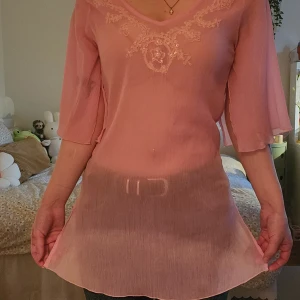 Rosa blus med broderi och v-ringning - Transparent rosa blus med v-ringad hals och broderade detaljer med paljetter framtill. Lätt och flödande material, samt små broderade blommor på både fram- och baksida. Finns små kaffedrickare på men inget som syns när den är på.