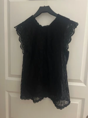 Svart spetsblus med volang - Säljer en svart blus med vackra spetsdetaljer och volangkant vid axlarna. 