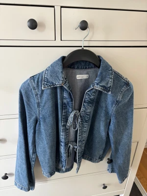 Blå jeansjacka med snörning XS - Använd fåtal ggr, aldrig tvättad. Snygg blå jeansjacka från Gina i storlek XS. Jackan har klassisk krage, långa ärmar och cool snörning framtill istället för dragkedja eller knappar. Perfekt för dig som gillar en chill och trendig look.