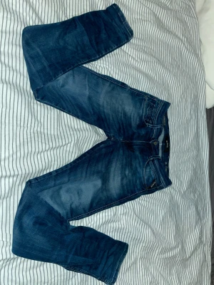 Replay Hyperflex Anbass jeans blå - Snygga Replay Hyperflex Anbass jeans i mörkblå tvätt med klassisk femficksdesign. Stretchigt material för extra komfort och smidig passform. Raka ben och normal midja, perfekt för dig som gillar stilrena och bekväma jeans.