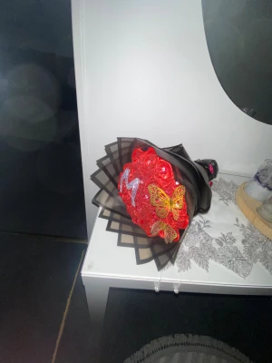 Glittrig röd ros-bukett med fjärilar - Unik bukett med glittriga röda rosor, dekorerad med en stor silvrig bokstav M i strass och två detaljerade guldfärgade fjärilar. Buketten är inslagen i svart och transparent papper som ger en cool kontrast. Perfekt som present eller dekoration!