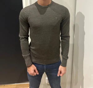 Stickad tröja - Snygg mörkgrå stickad tröja från Brunn & Stengade med diskret logga på bröstet. Tröjan har rund hals, ribbade muddar och är långärmad. Passformen är normal och materialet känns mjukt och skönt mot huden. Perfekt för dig som gillar stilrena och klassiska plagg.