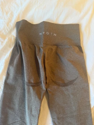 leggings från NVGTN - Mörkbruna leggings från NVGTN med hög midja och tight passform. Tillverkade i stretchigt syntetmaterial som sitter skönt och formar sig efter kroppen. Perfekta för gymmet eller chill hemma. Diskret logga bak i midjan.