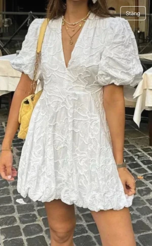 Vit kort klänning med puffärm och blommor - Supersöt vit kort klänning från Zara med puffiga ärmar och v-ringning. Klänningen har broderade blommor över hela tyget och en ballongformad nederkant som ger en unik look. Perfekt för dig en sommar fest eller studenten!! Andvänd en gång!