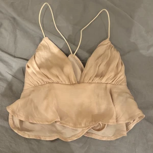 Beige omlott linnetopp med volang - Säljer en ljusbeige linnetopp med tunna axelband och omlott-design. Toppen har en v-ringad skärning och volangdetalj nedtill som ger en romantisk vibe. Perfekt för varma dagar och sommarhäng. Materialet känns lätt och luftigt.