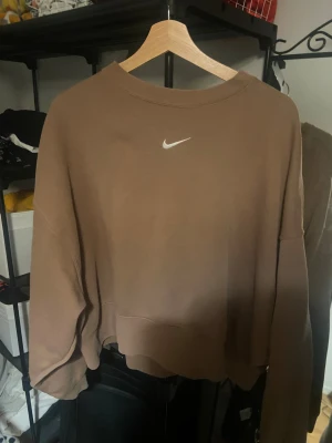 Brun Nike sweatshirt i storlek L - Säljer en brun sweatshirt från Nike i storlek L. Tröjan har en enkel design med Nike-loggan broderad i vitt på bröstet. Den är långärmad och har en loose passform med ribbade muddar vid hals, ärmslut och nederkant. Perfekt för chill dagar.