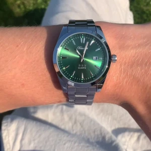 Grön och silverfärgad klocka från Doventi  - Snygg klocka från Doventi med grön urtavla och datumvisning. Klockan har ett stilrent, runt hölje i silverfärgad metall och matchande länkarmband. Quartz-urverk och minimalistiska indexmarkeringar ger en modern vibe. Perfekt accessoar för dig som gillar att sticka ut.